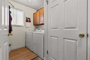 Laundry area with washer and dryer, light wood-type flooring, and cabinet space