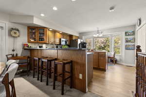Kitchen with wood finish cabinetry, a peninsula, dark countertops, hanging lights, and glass insert cabinets