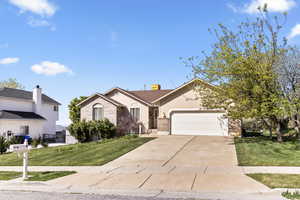 View of front of property featuring an attached garage, brick siding, concrete driveway, and a front lawn