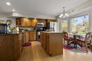 Kitchen with wood finish cabinets, stainless steel appliances, a chandelier, light wood-style floors, and glass fronted cabinets