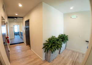 Hallway with light wood-style flooring, recessed lighting, and elevator