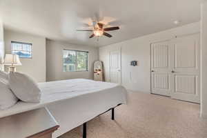 Bedroom featuring light colored carpet, a ceiling fan, and multiple closets