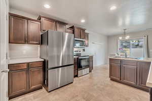 Kitchen featuring stainless steel appliances, light countertops, suspended lighting, and dark wood finish cabinetry