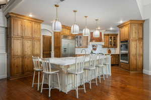 Kitchen with a breakfast bar area, wood finish cabinetry, light stone countertops, glass fronted cabinets, and a large island