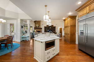 Kitchen featuring built in appliances, open floor plan, decorative light fixtures, a fireplace, and dark wood-type flooring