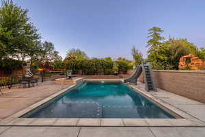 Integrated pool / hot tub with a patio, a fenced backyard, and a water slide