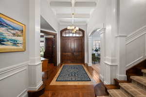 Foyer entrance with arched walkways, coffered ceiling, wainscoting, dark wood-type flooring, and a decorative wall