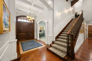 Entryway with arched walkways, a decorative wall, dark wood finished floors, coffered ceiling, and suspended lighting