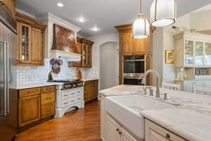 Two tone kitchen with glass insert cabinets, light stone countertops, stainless steel appliances, backsplash, and two tone cabinetry