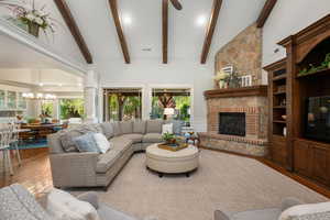 Living area featuring wood-type flooring, lofted ceiling, a large fireplace, decorative columns, and suspended lighting