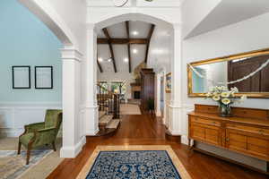 Foyer entrance featuring wood-type flooring, a wainscoted wall, a decorative wall, arched walkways, and a fireplace with raised hearth