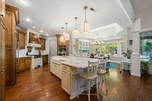 Kitchen with glass insert cabinets, two tone color scheme, a large island with sink, light stone countertops, and a breakfast bar area