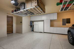 Garage with electric panel, a garage door opener, and freestanding refrigerator