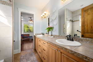 Bathroom with double vanity, a tile shower, a ceiling fan, and light tile patterned floors