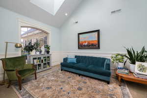 Living area with wainscoting, a decorative wall, lofted ceiling, a skylight, and carpet floors