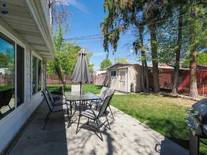 Fenced backyard with a patio area, outdoor dining space, and a storage shed