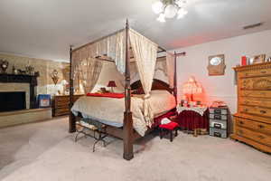 Bedroom featuring light carpet, a fireplace with raised hearth, and a textured ceiling