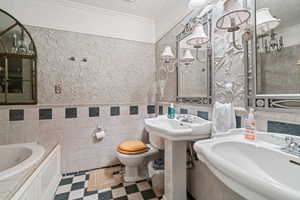 Full bathroom with two sinks, wainscoting, ornamental molding, a bath, and tile walls