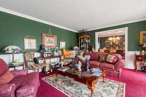 Living area featuring a chandelier, carpet floors, crown molding, and wainscoting