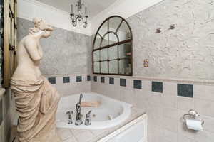 Full bathroom featuring a tub with jets, crown molding, wainscoting, a textured wall, and tile walls