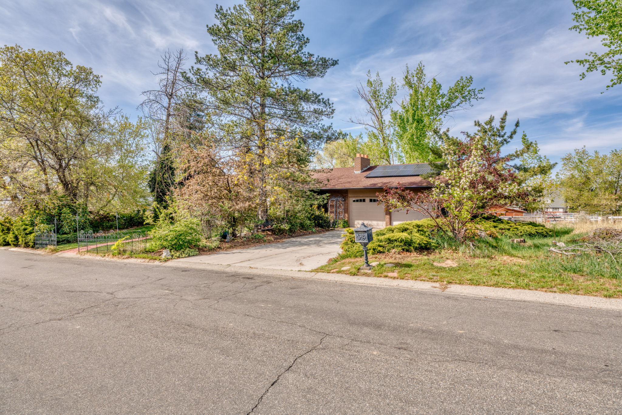 View of property hidden behind natural elements featuring roof mounted solar panels, driveway, a chimney, and an attached garage