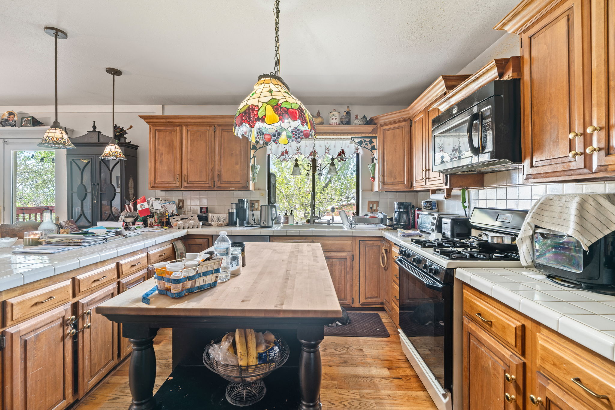 Kitchen with tile counters, black appliances, wood finish cabinetry, light wood finished floors, and plenty of natural light