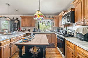 Kitchen with tile counters, black appliances, wood finish cabinetry, light wood finished floors, and plenty of natural light