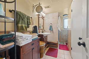 Bathroom featuring a shower stall, vanity, light tile patterned flooring, tile walls, and a textured wall