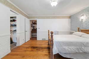 Bedroom featuring hardwood / wood-style floors, ceiling fan, crown molding, and wallpapered walls