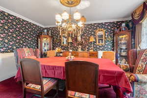 Dining space featuring ornamental molding, wallpapered walls, a chandelier, and carpet