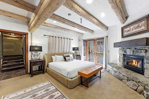Bedroom featuring beamed ceiling, french doors, a stone fireplace, access to outside, and recessed lighting