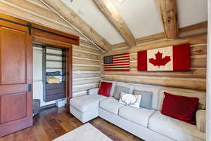 Living area featuring rustic walls, dark wood finished floors, a barn door, and beamed ceiling