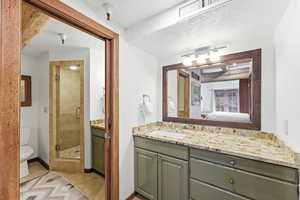 Ensuite bathroom featuring vanity, a shower stall, a textured ceiling, and light tile patterned flooring