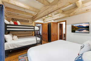 Bedroom with rustic walls, dark wood-type flooring, and beam ceiling