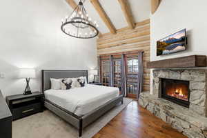 Bedroom featuring rustic walls, light wood-type flooring, a fireplace, lofted ceiling, and suspended lighting