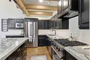 Kitchen featuring premium appliances, decorative backsplash, light wood-style floors, light stone counters, and beam ceiling