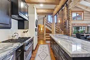 Kitchen featuring light stone counters, high end stove, rustic walls, tasteful backsplash, and dark wood-style floors
