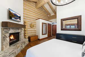 Bedroom with log walls, dark wood-style floors, a fireplace, vaulted ceiling, and hanging lights