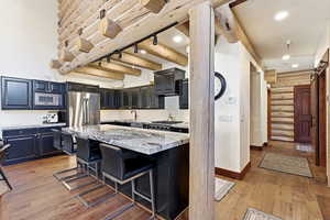 Kitchen featuring a barn door, a kitchen island, light stone countertops, a kitchen breakfast bar, and light wood-style floors
