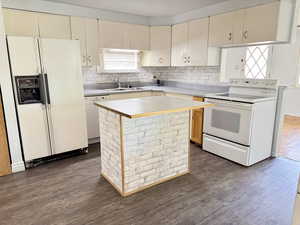 Kitchen with white appliances, dark wood-type flooring, a kitchen island, cream cabinets, and tasteful backsplash
