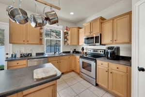 Kitchen with dark countertops, light wood finish cabinets, stainless steel appliances, open shelves, and recessed lighting