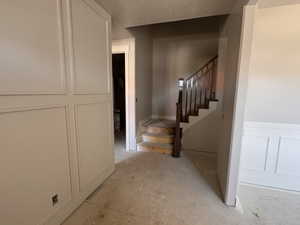 Interior entryway featuring a wooden staircase with a dark wood handrail and balusters, wainscoting details, and light-toned wall finishes