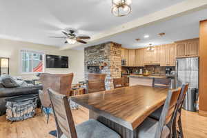 Dining area with light wood finished floors, a ceiling fan, a fireplace, and beamed ceiling