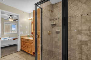 Ensuite bathroom featuring vanity, a stall shower, light tile patterned floors, and a ceiling fan