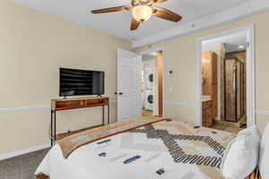 Bedroom featuring stacked washer and clothes dryer, ceiling fan, ensuite bathroom, and light colored carpet