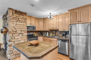 Kitchen featuring stainless steel appliances, light wood finish cabinetry, decorative backsplash, a kitchen island, and light wood finished floors