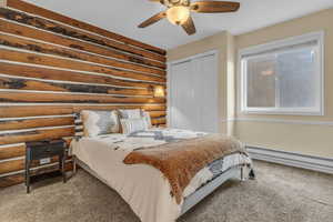 Bedroom with rustic walls, carpet flooring, ceiling fan, a closet, and baseboard heating