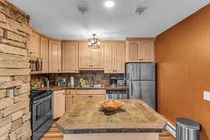 Kitchen with a kitchen island, light wood-style flooring, stainless steel appliances, tile counters, and light wood finish cabinetry