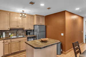 Kitchen with a kitchen island, stainless steel appliances, tile countertops, backsplash, and light wood finish cabinets