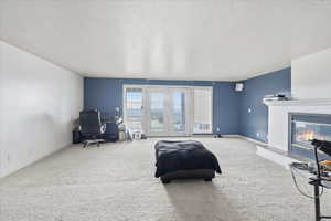 Carpeted living area with a textured ceiling, french doors, a glass covered fireplace, and an office area